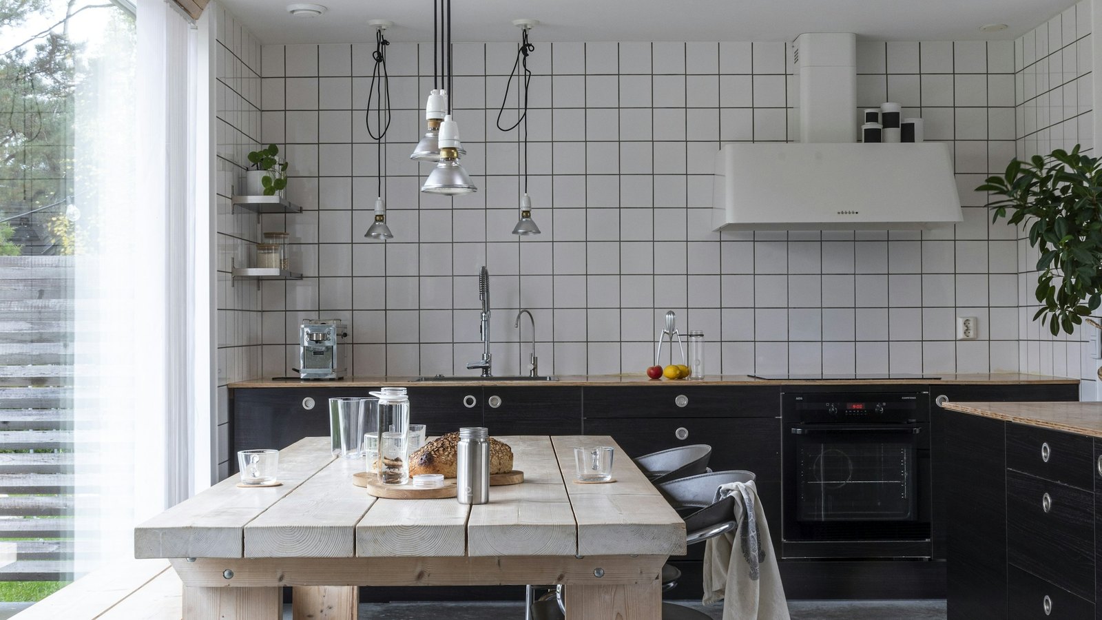 Skandinavisk kjøkken med langbord i lyst tre ved vinduet, dekket til frokost.