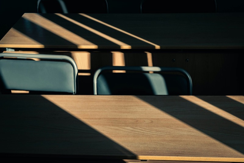 Sollys gjennom persienner faller i striper over tomme skolepulter.