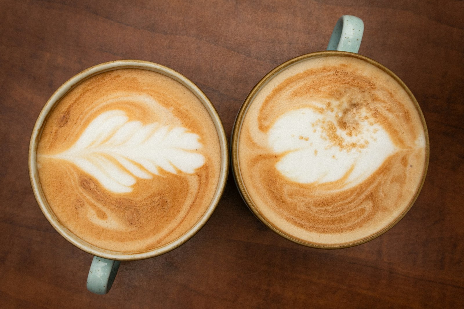 To like kaffekopper side om side på et mørkt trebord, sett ovenfra.